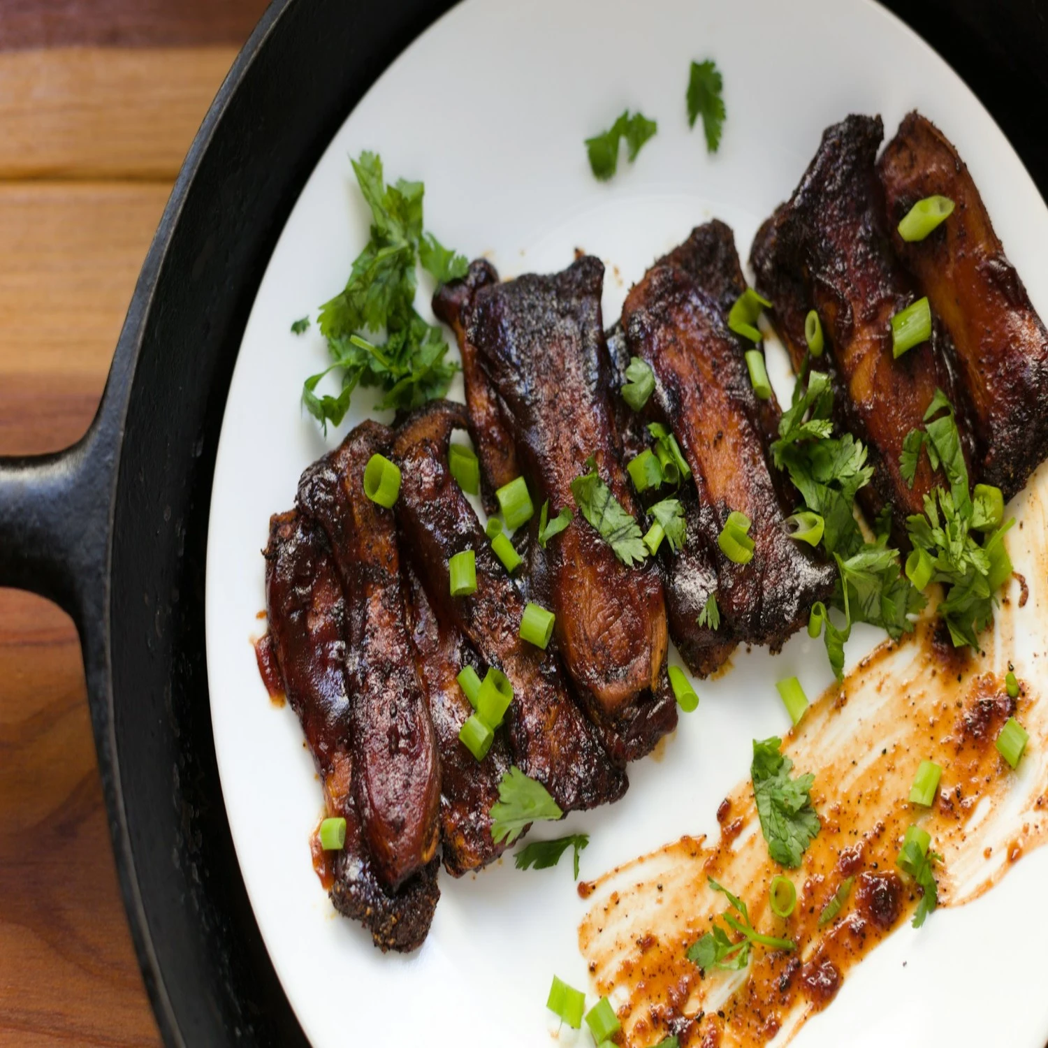 a ceramic plate of dry ribs with a coat of sauce in the bottom part of the plate and freshly cut green onios on top of the ribs