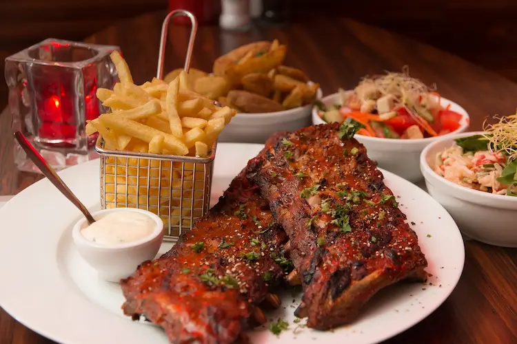 a plate of ribs and fries with sides dishes surronding them